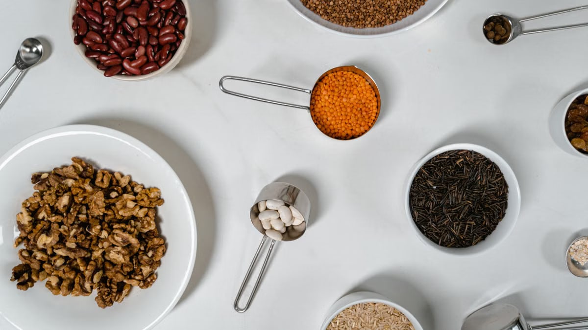 Flat lay of assorted grains, seeds, and nuts in bowls and cups on a white surface.